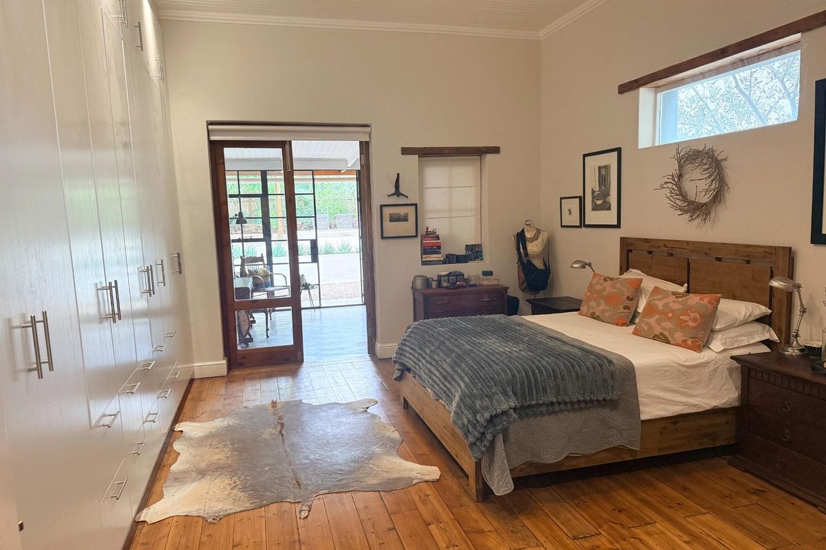 Spacious bedroom featuring polished timber flooring, extensive floor-to-ceiling built-in cabinetry, and direct access to an outdoor patio area through glass-paneled doors.