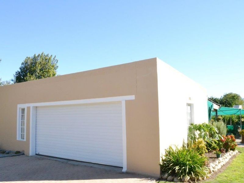 A detached garage building featuring a white roller door, smooth rendered exterior walls, and a paved driveway area.
