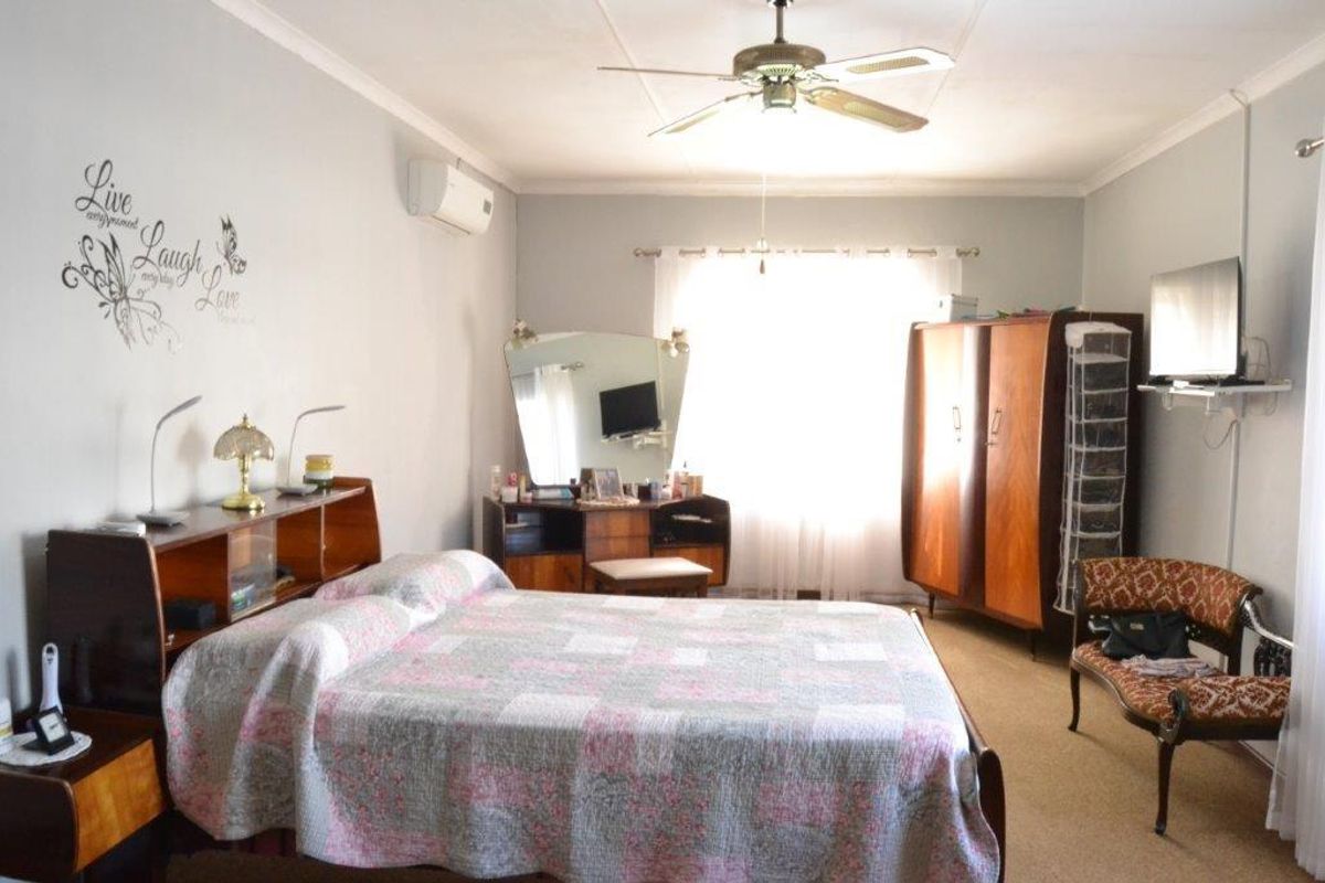 A spacious bedroom featuring a ceiling fan, wall-mounted air conditioning unit, and neutral wall finishes.