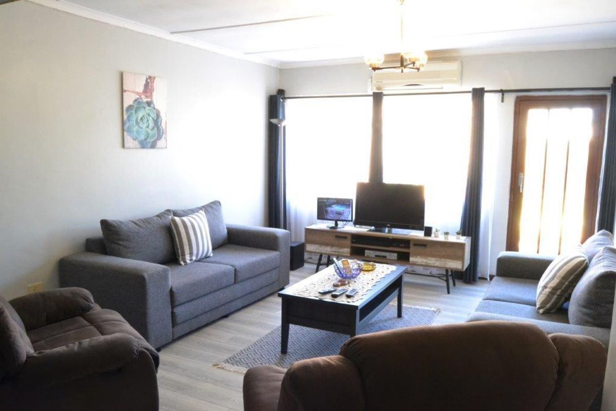 A comfortable living room featuring light-toned laminate flooring, a wall-mounted air conditioning unit, and direct access to an outdoor area via a glass-paneled door.