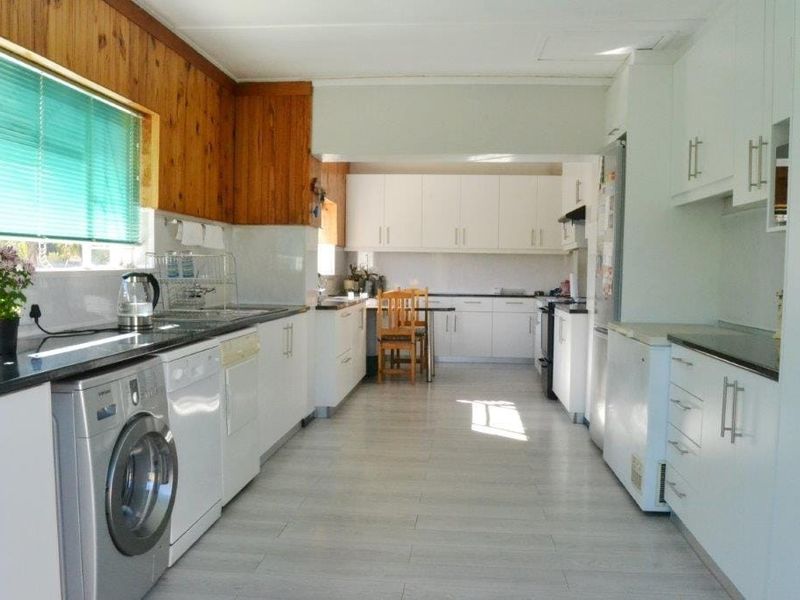 A functional kitchen featuring white cabinetry, laminate countertops, tiled flooring, and integrated laundry plumbing, offering a clean and practical workspace.