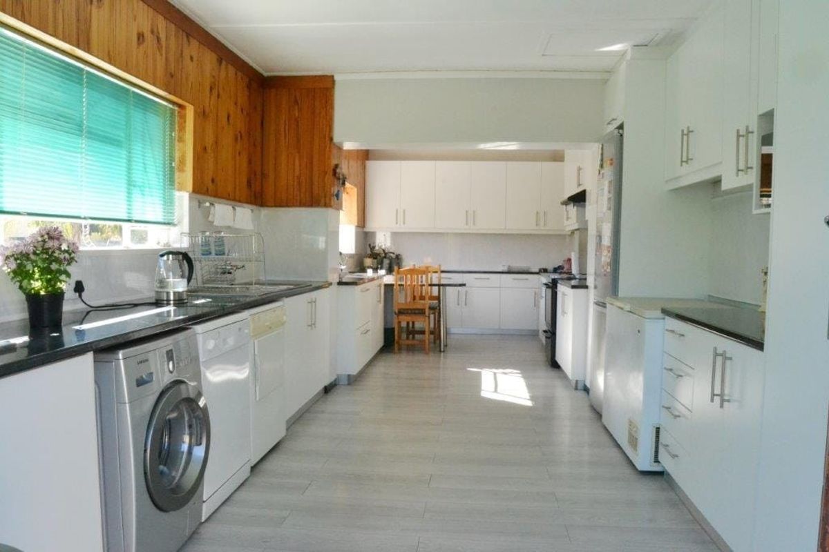 A functional kitchen featuring white cabinetry, laminate countertops, tiled flooring, and integrated laundry plumbing, offering a clean and practical workspace.