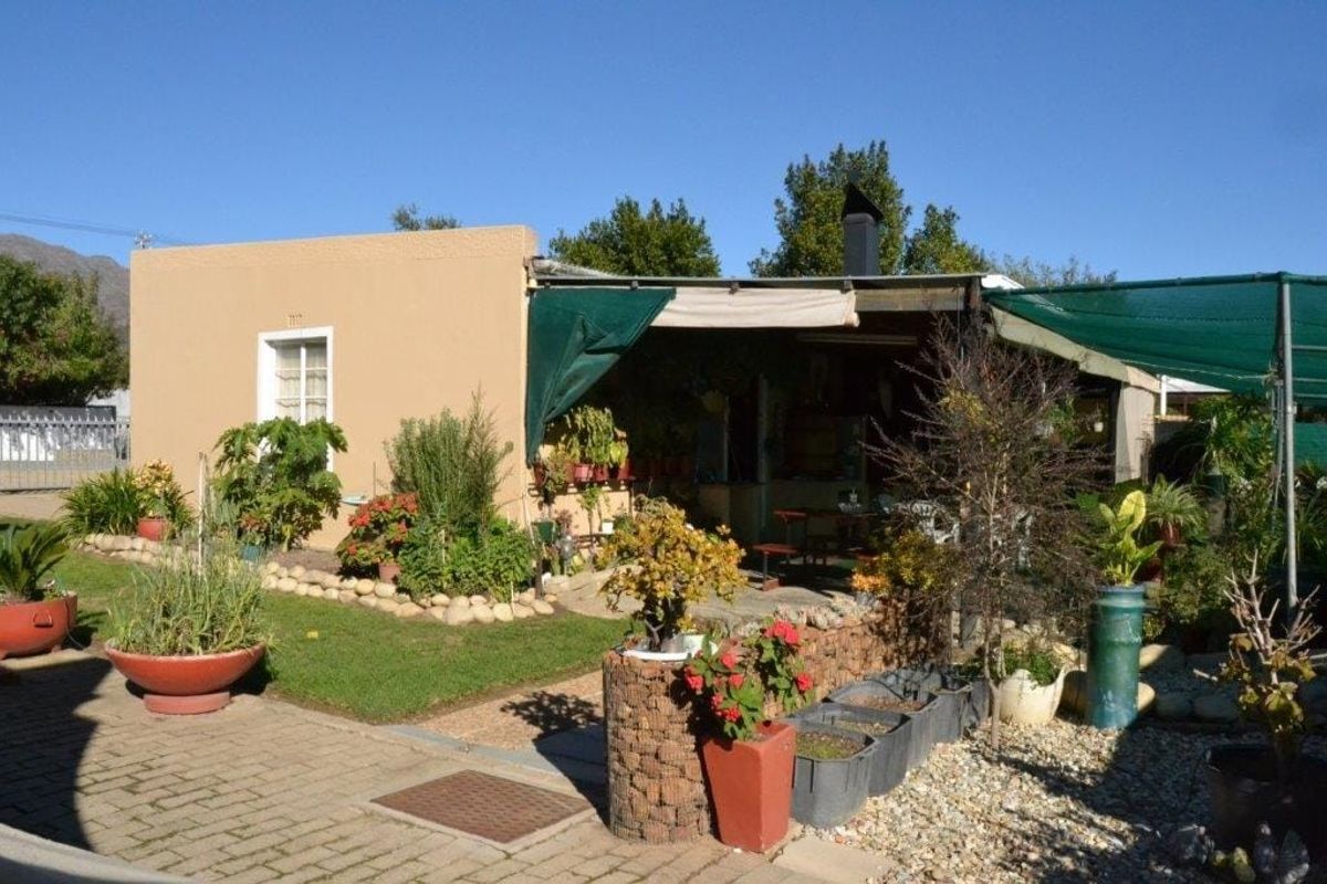 Rear exterior view featuring a covered patio area with a built-in braai, paved ground, and landscaped garden elements.