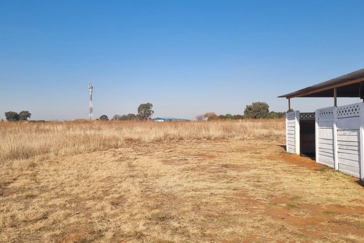 An exterior view of a farm property featuring a simple white-painted structure with a corrugated metal roof set against an expansive open field.