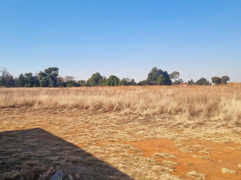 A wide, open expanse of undeveloped farm land featuring dry grass and natural terrain under a clear blue sky.