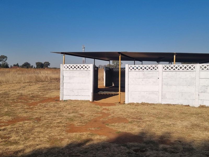 A simple outdoor utility structure featuring precast concrete wall panels and a metal roof, situated on open farm land.