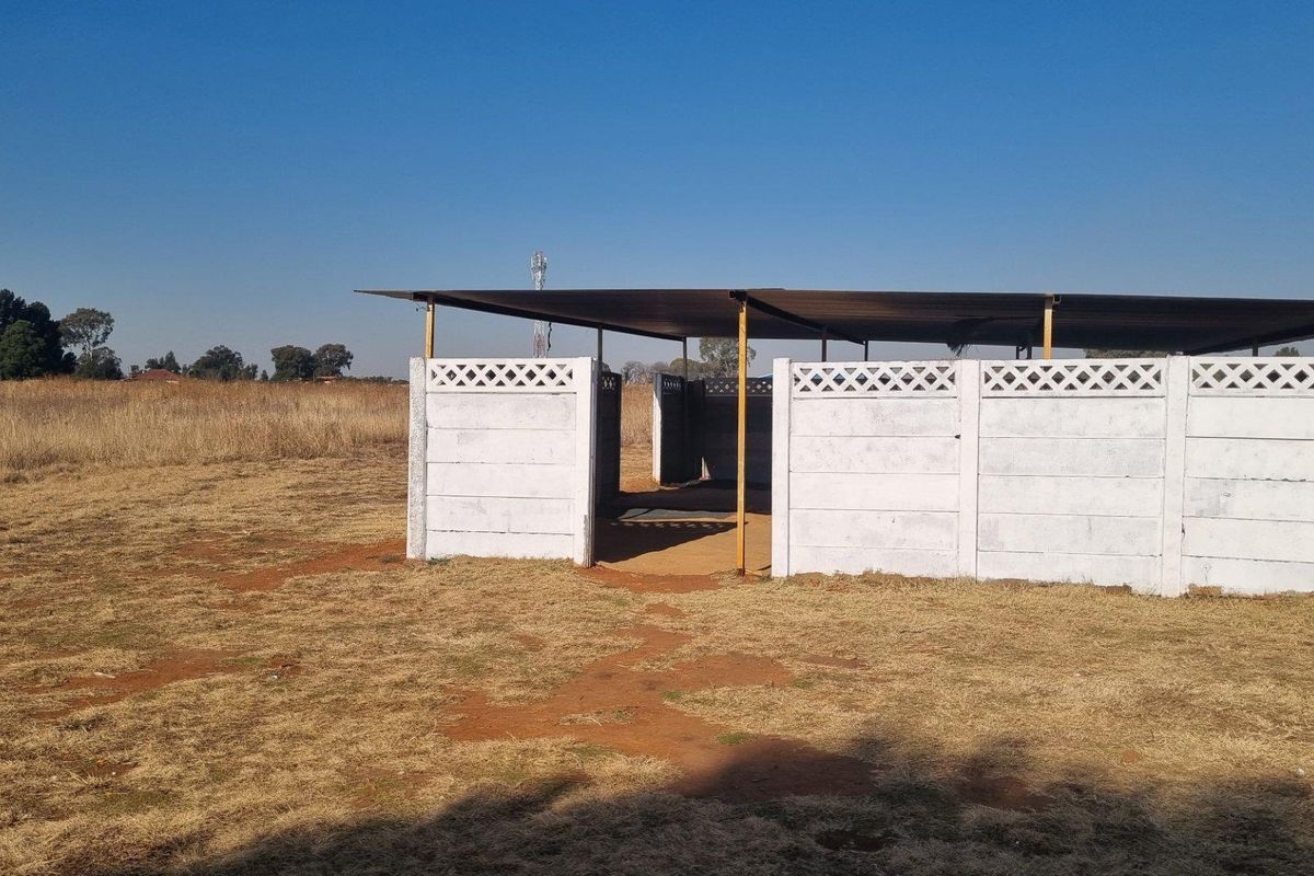 A simple outdoor utility structure featuring precast concrete wall panels and a metal roof, situated on open farm land.