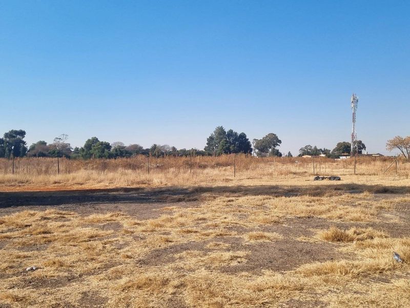 An expansive, undeveloped plot of land featuring dry grass, perimeter fencing, and a clear view of the surrounding rural landscape.