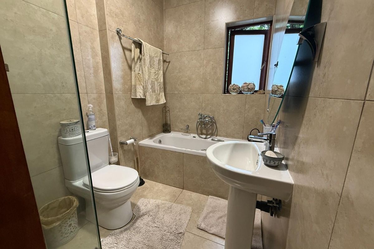 A functional bathroom featuring floor-to-ceiling beige tiling, a pedestal basin, a built-in bathtub, and a separate glass-enclosed shower area.
