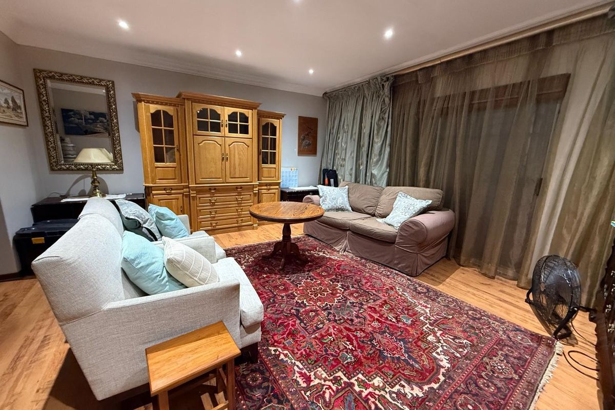 A comfortable living room featuring warm wood-look flooring, recessed ceiling lighting, and large sliding glass doors with floor-to-ceiling curtains.