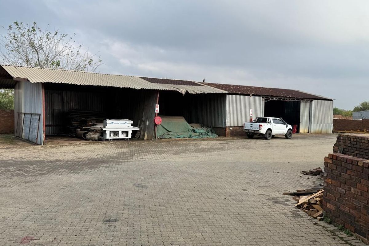 Industrial property featuring a large open-sided storage shed with corrugated metal roofing and siding, set on a paved yard area.