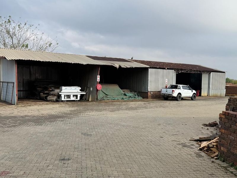 Industrial property featuring a large open-sided storage shed with corrugated metal roofing and siding, set on a paved yard area.