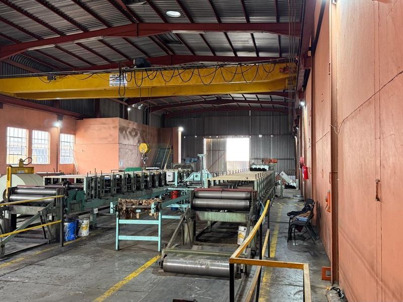Industrial warehouse space featuring a high-clearance ceiling, overhead gantry crane, and integrated heavy-duty manufacturing machinery for industrial operations.