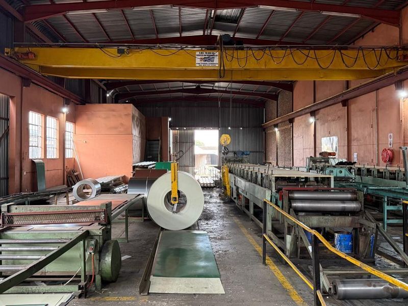 Spacious industrial warehouse facility featuring a high-clearance ceiling, overhead gantry crane, and integrated metal processing machinery for manufacturing operations.