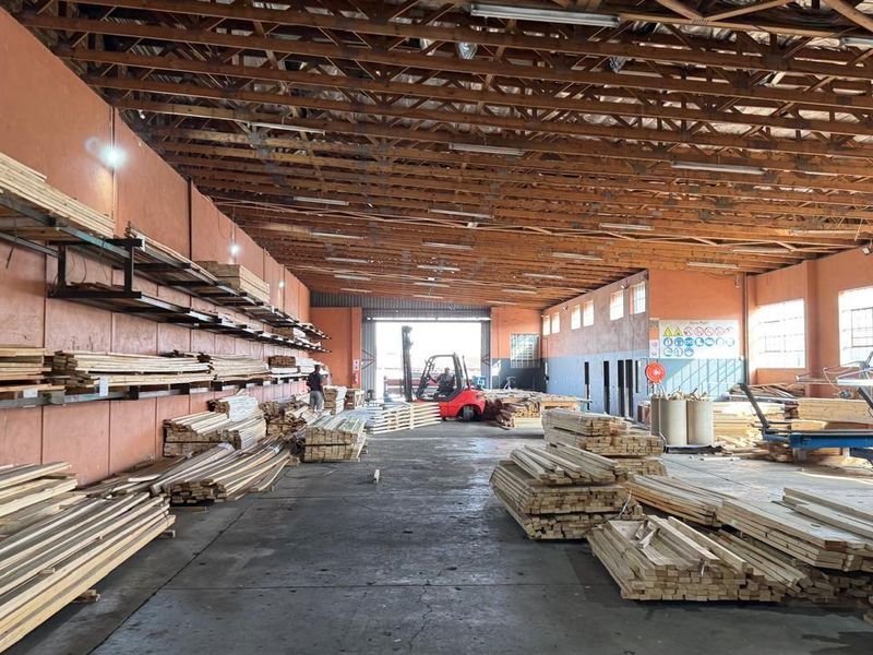 Spacious industrial warehouse featuring high exposed timber truss ceilings, concrete flooring, and integrated wall-mounted storage racking for materials.