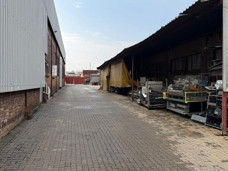 Industrial exterior yard space featuring paved ground, corrugated metal cladding, and covered storage areas between warehouse structures.