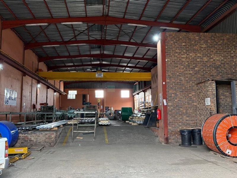 Spacious industrial warehouse featuring high ceilings, exposed steel trusses, an overhead crane system, and brick wall accents, suitable for manufacturing or storage operations.