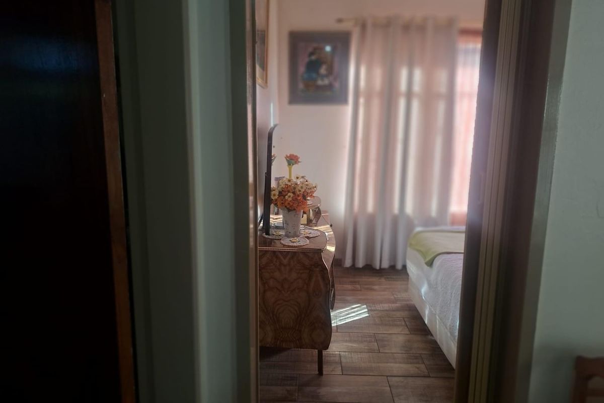 A view into a bedroom featuring wood-look tile flooring and natural light filtering through curtains.
