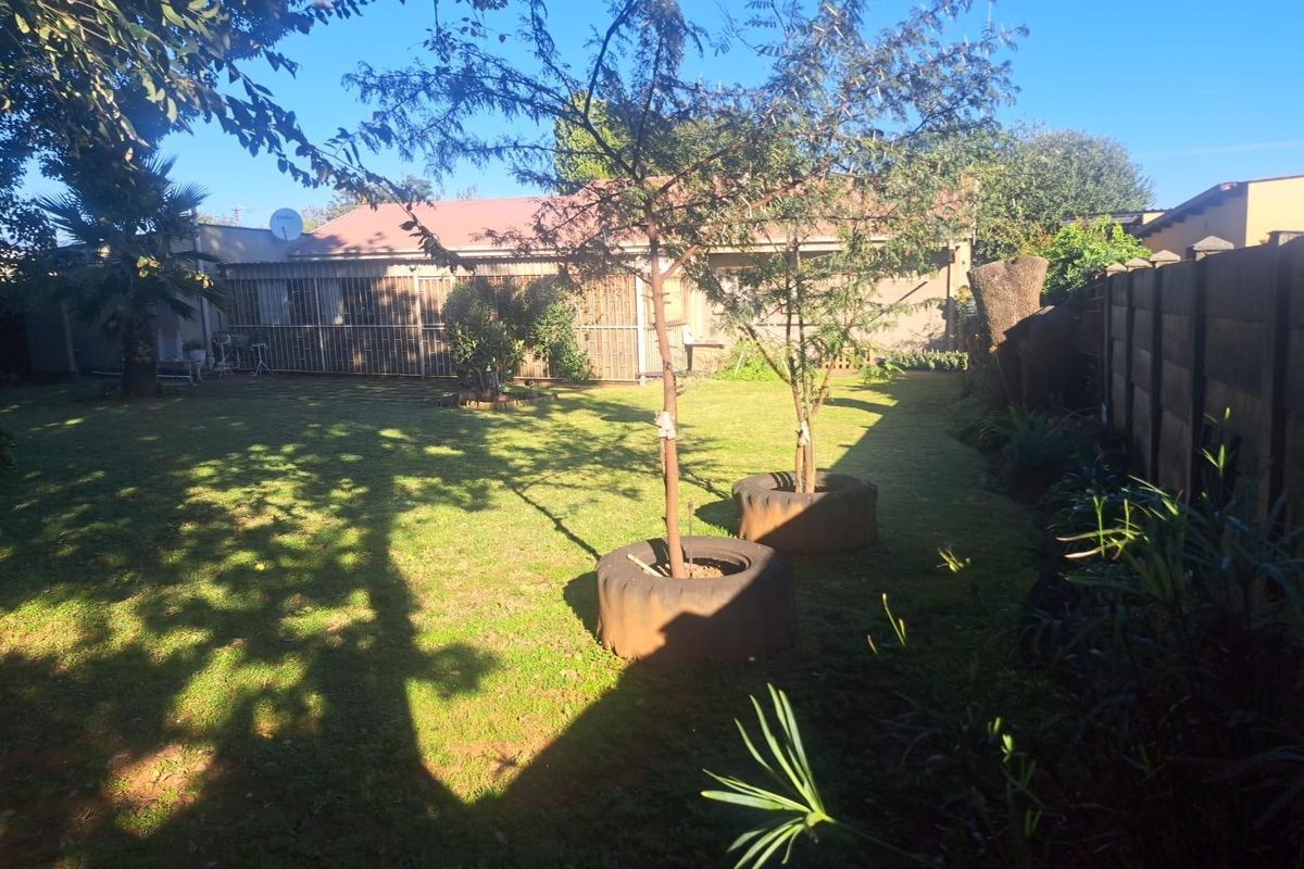 A spacious rear garden featuring a well-maintained lawn, mature trees, and a secure perimeter wall, providing a private outdoor area.