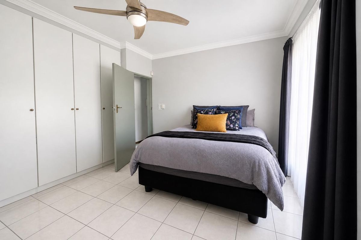 A bright bedroom featuring built-in floor-to-ceiling wardrobes, tiled flooring, and a modern ceiling fan.