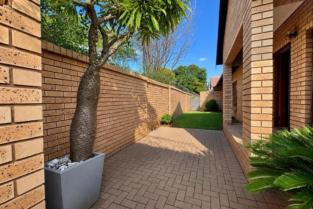 A private side garden area featuring paved walkways, face-brick boundary walls with security razor wire, and a well-maintained lawn.