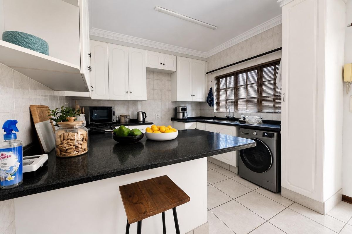 A functional kitchen featuring white cabinetry, dark granite countertops, tiled backsplash, and an integrated washing machine space.