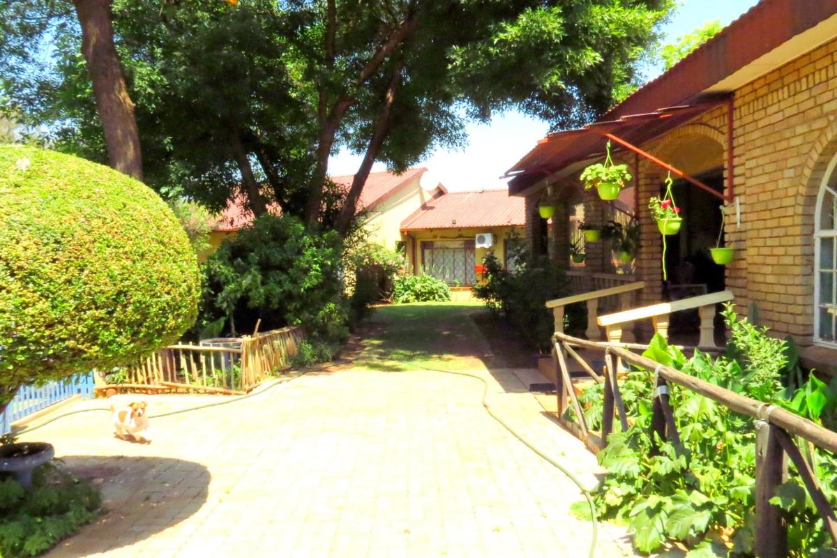 A view of the farm property featuring a brick facade, covered patio area, and established garden surroundings with paved pathways.