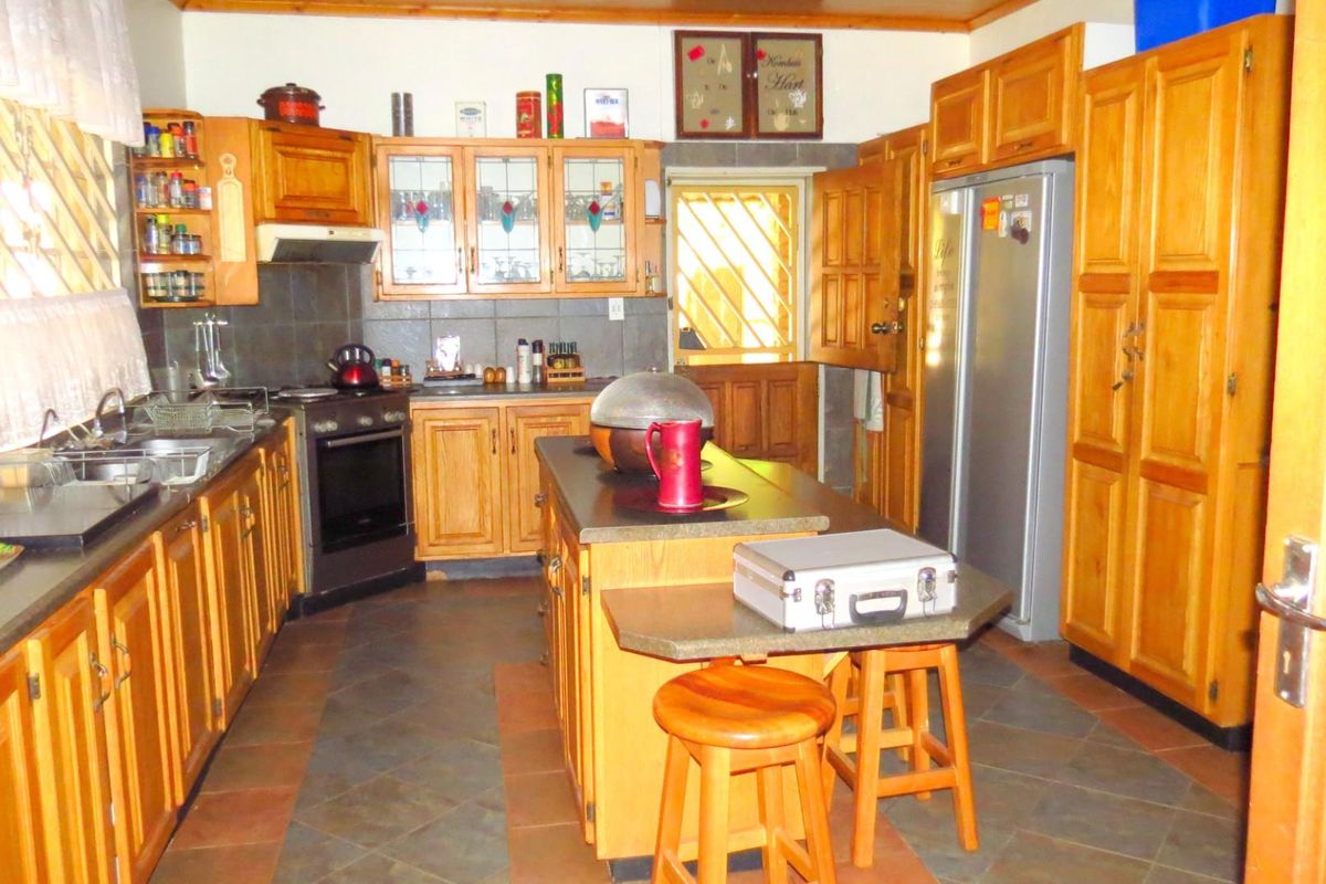 A traditional farm-style kitchen featuring extensive wooden cabinetry, a central island, dark stone countertops, and a built-in oven with extractor fan.