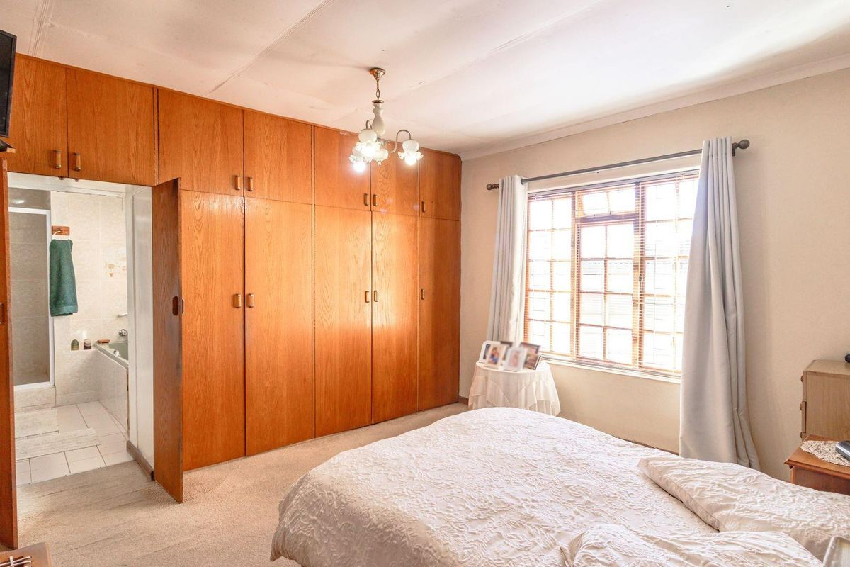 Spacious bedroom featuring extensive built-in wooden cabinetry, large window with natural light, and an en-suite bathroom access.