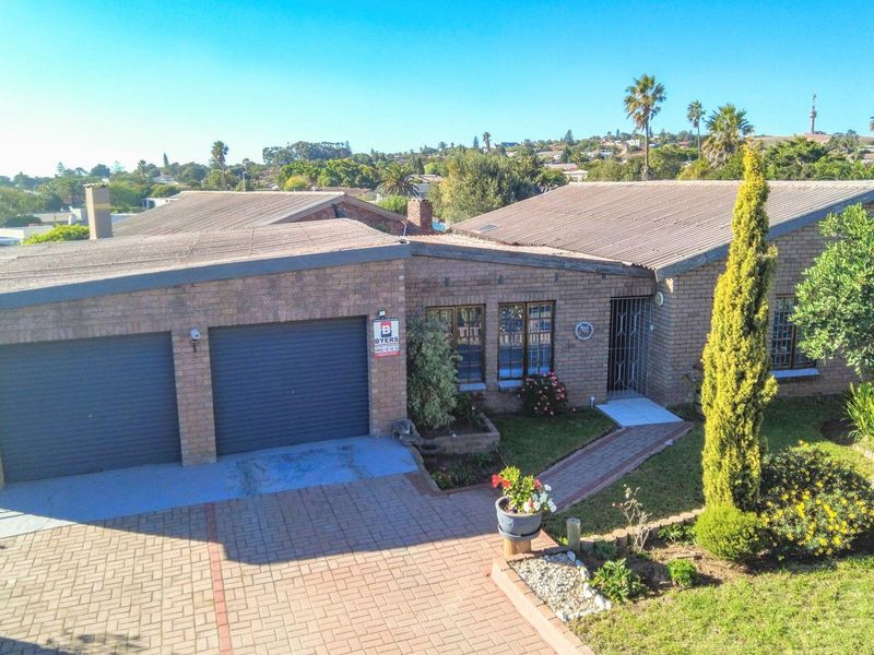 Aerial view of a brick-faced residential property featuring a double garage, paved driveway, and established front garden in a suburban setting.