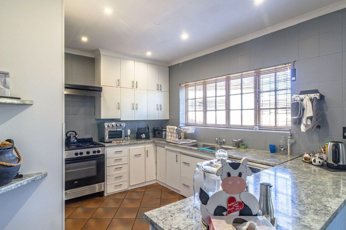 A functional kitchen featuring white cabinetry, granite-style countertops, a gas stove with extractor fan, and a double sink under a window.