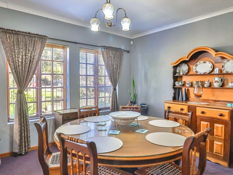 A well-lit dining room featuring large windows with fitted blinds, coved ceilings, and neutral wall finishes.