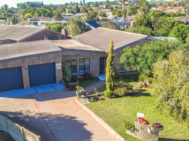 Aerial view of a brick-faced residential house featuring a double garage, paved driveway, and established front garden in a suburban neighborhood.