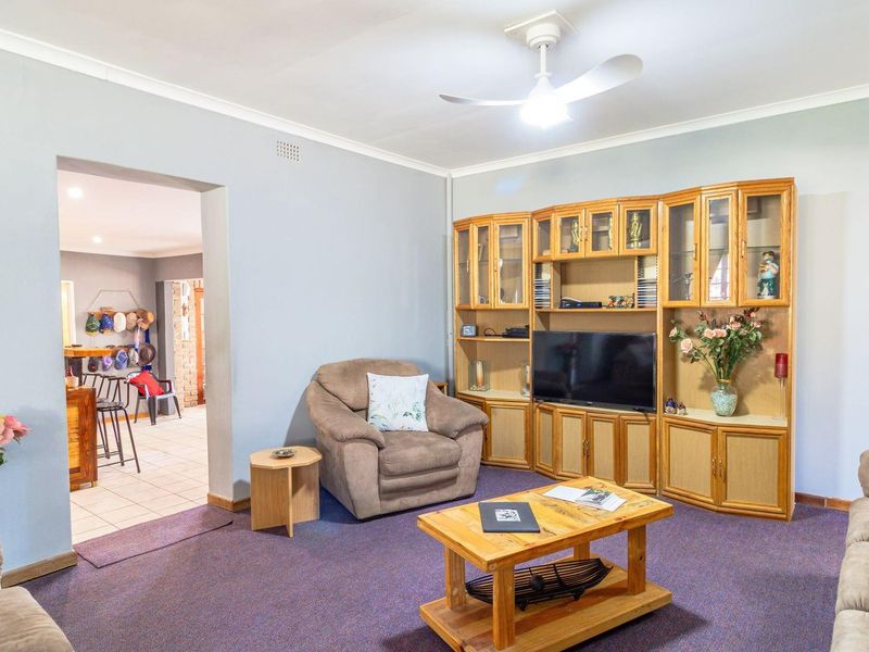 A comfortable living room featuring built-in wooden cabinetry and a ceiling fan, with an open-plan transition into the adjacent kitchen area.