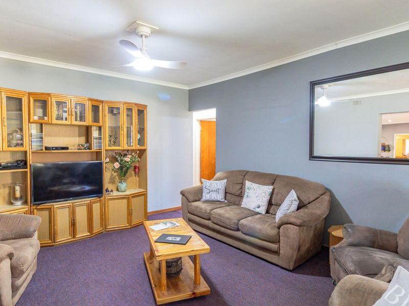 A living room featuring a built-in wooden wall unit, ceiling fan, and carpeted flooring.