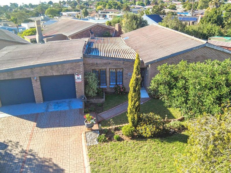 Aerial view of a brick-faced residential property featuring a double garage, paved driveway, and established front garden in a suburban neighborhood.