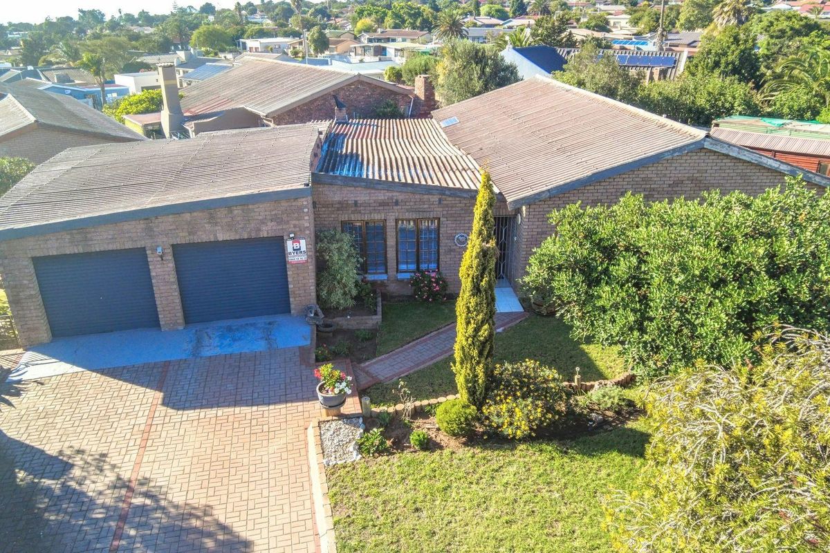 Aerial view of a brick-faced residential property featuring a double garage, paved driveway, and established front garden in a suburban neighborhood.