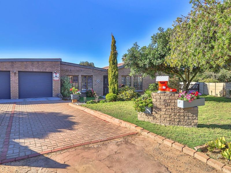 Front view of a brick-faced house featuring a double garage, paved driveway, and established front garden with a brick boundary wall.
