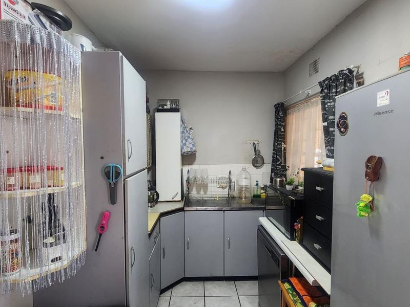 A compact kitchen featuring grey cabinetry, tiled flooring, and a functional layout with integrated sink and storage space.