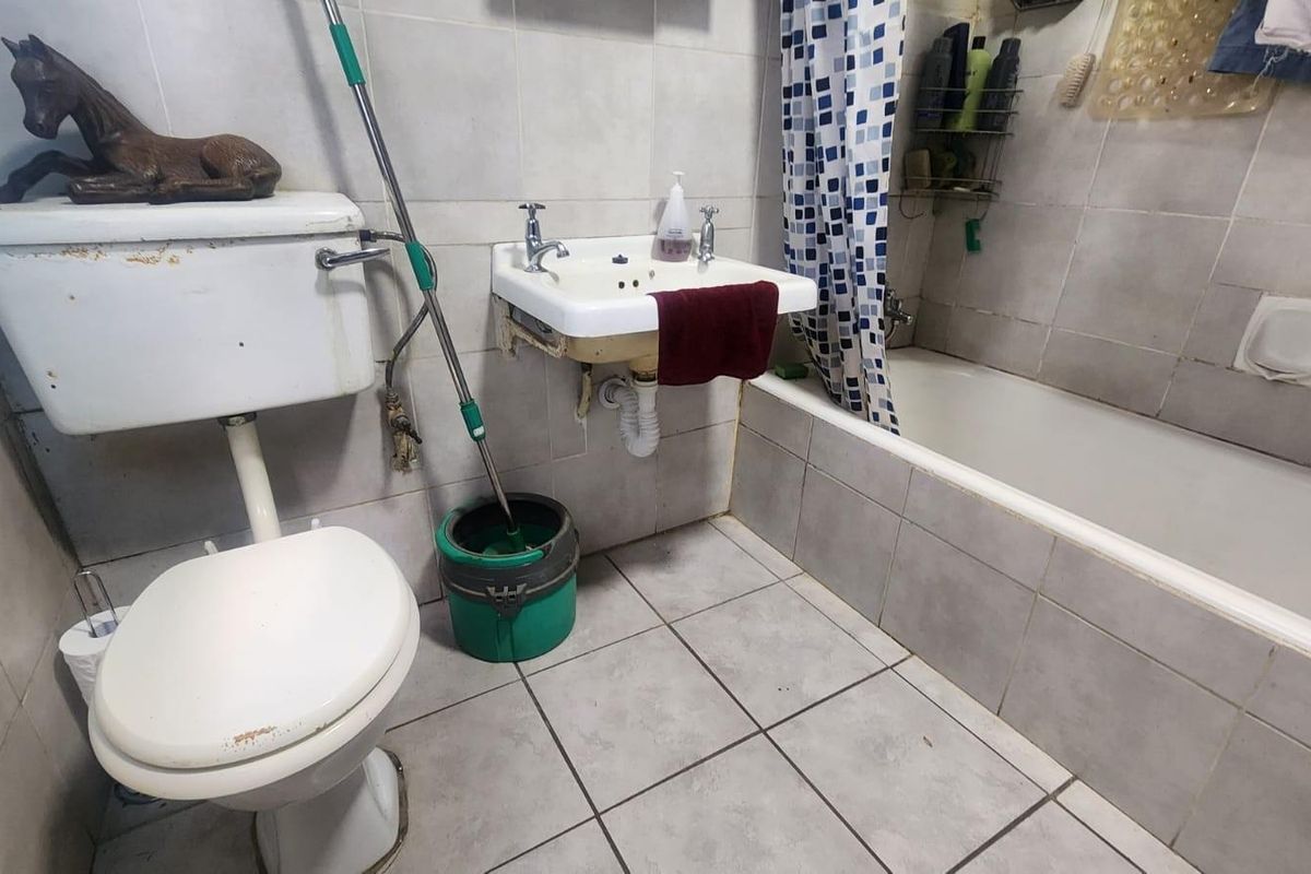 A dated bathroom featuring a wall-mounted sink, a standard toilet, and a tiled bathtub with a shower curtain.
