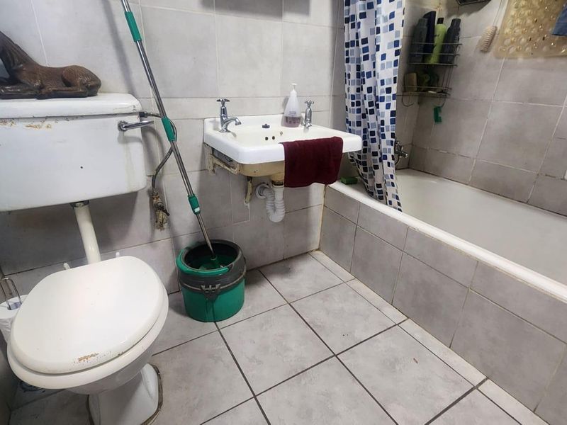 A dated bathroom featuring a wall-mounted sink, a standard toilet, and a tiled bathtub with a shower curtain.