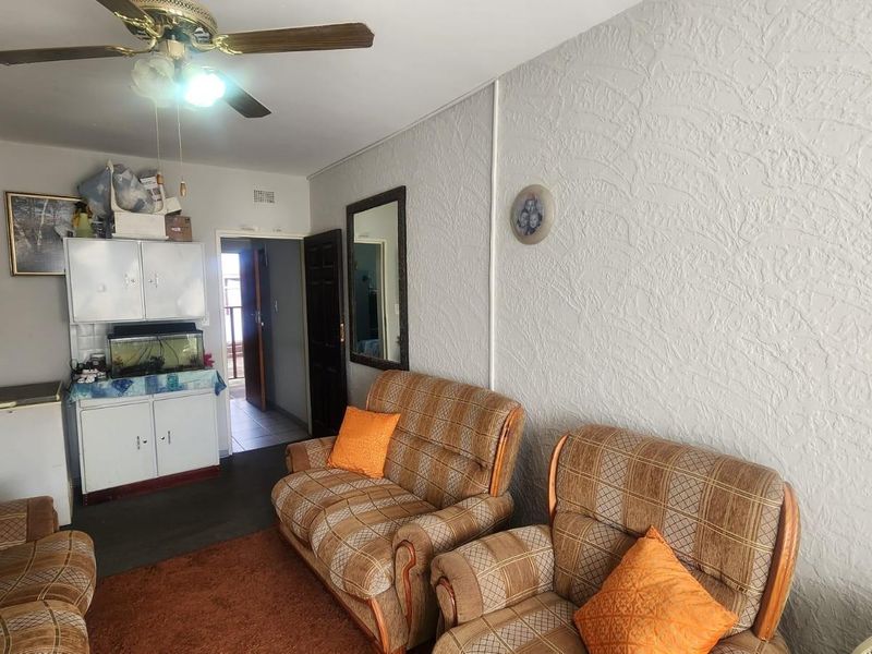 A living room area featuring a ceiling fan, textured walls, and access to an adjacent hallway.