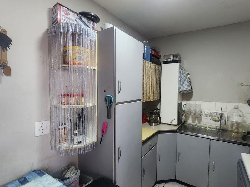 A compact kitchen featuring grey cabinetry, a stainless steel sink, and tiled splashbacks, offering a functional layout for daily meal preparation.