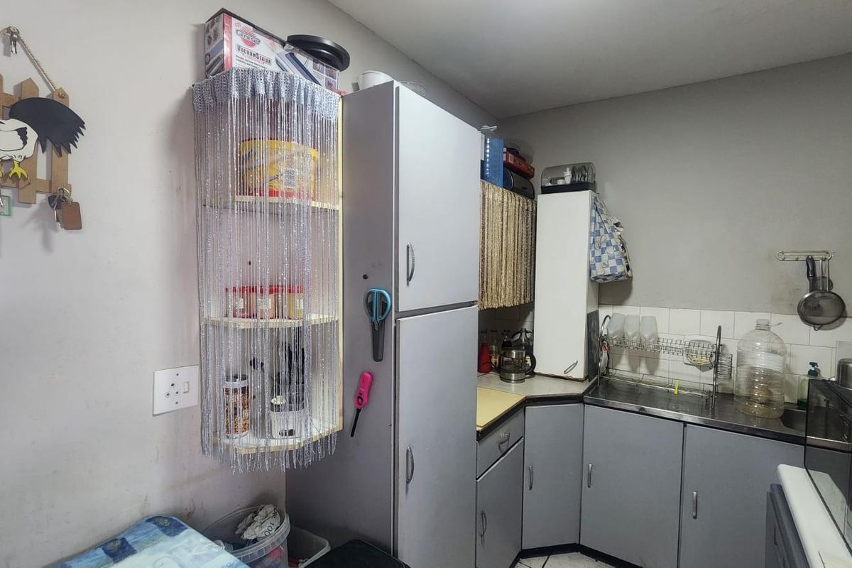 A compact kitchen featuring grey cabinetry, a stainless steel sink, and tiled splashbacks, offering a functional layout for daily meal preparation.