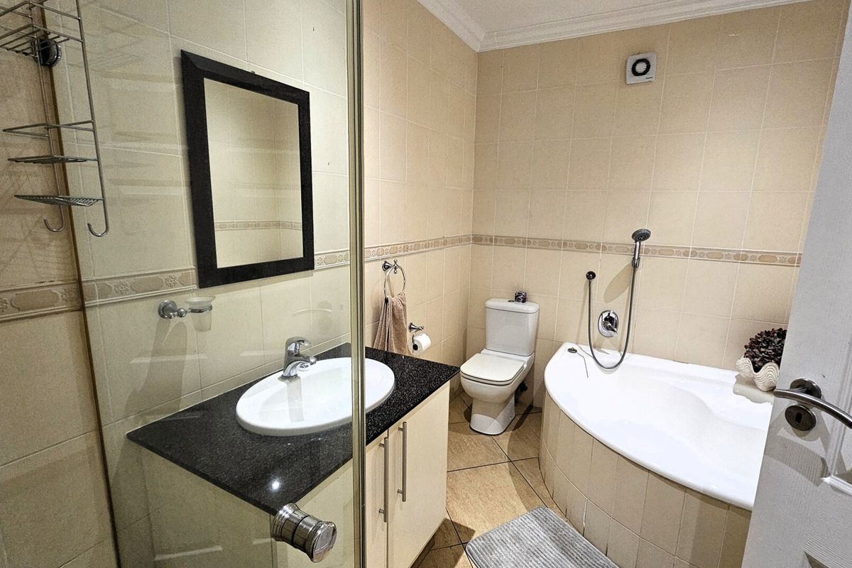 A functional bathroom featuring a vanity with granite countertop, a corner bathtub with handheld shower attachment, and a separate glass-enclosed shower area.
