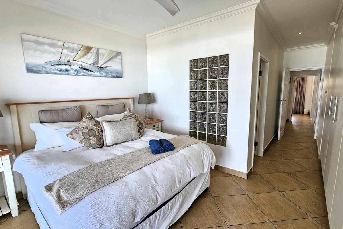 A well-maintained bedroom featuring tiled flooring, built-in cupboards, and a decorative glass block feature wall, leading into a hallway.