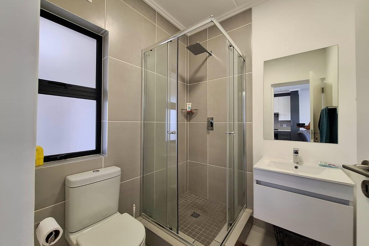 Modern bathroom featuring a glass-enclosed shower, wall-mounted vanity with basin, and a contemporary toilet, finished with neutral wall tiles.
