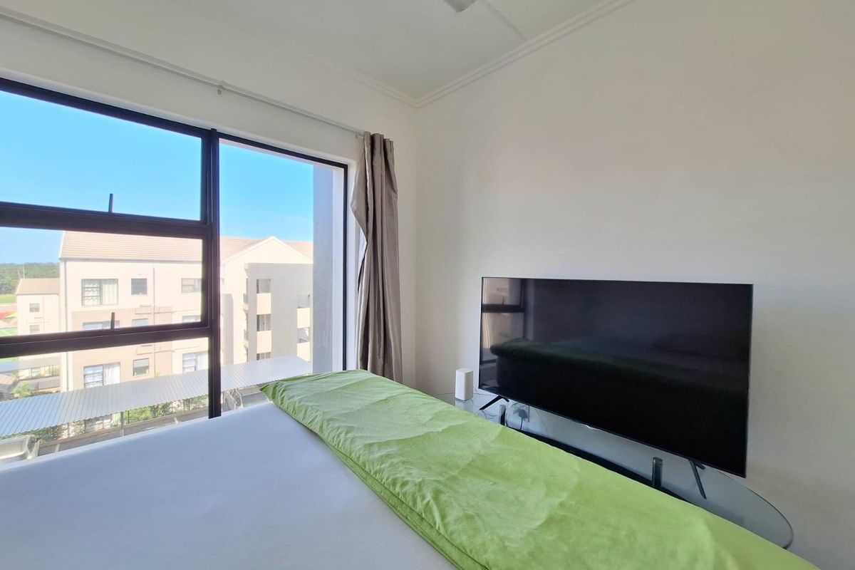 A bright bedroom featuring large windows with natural light and views of the surrounding apartment complex.