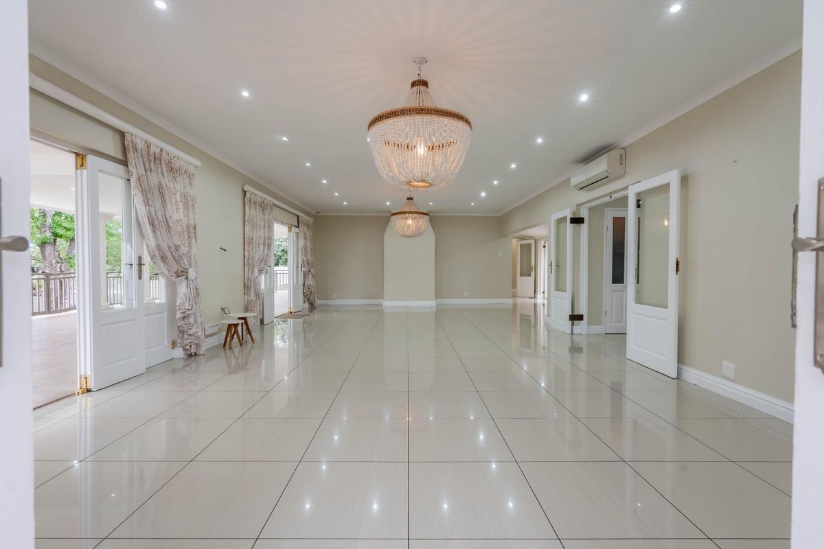 Spacious, light-filled living area featuring polished porcelain floor tiles, recessed downlighting, elegant chandeliers, and multiple glass-paneled doors opening to an outdoor patio.