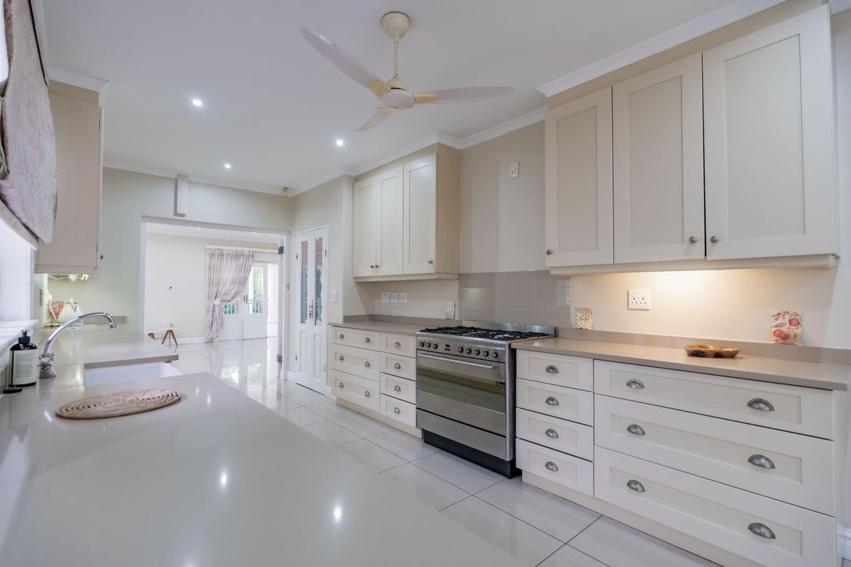 A well-appointed kitchen featuring shaker-style cabinetry, stone countertops, a stainless steel gas range, and integrated lighting, leading into an adjacent living area.